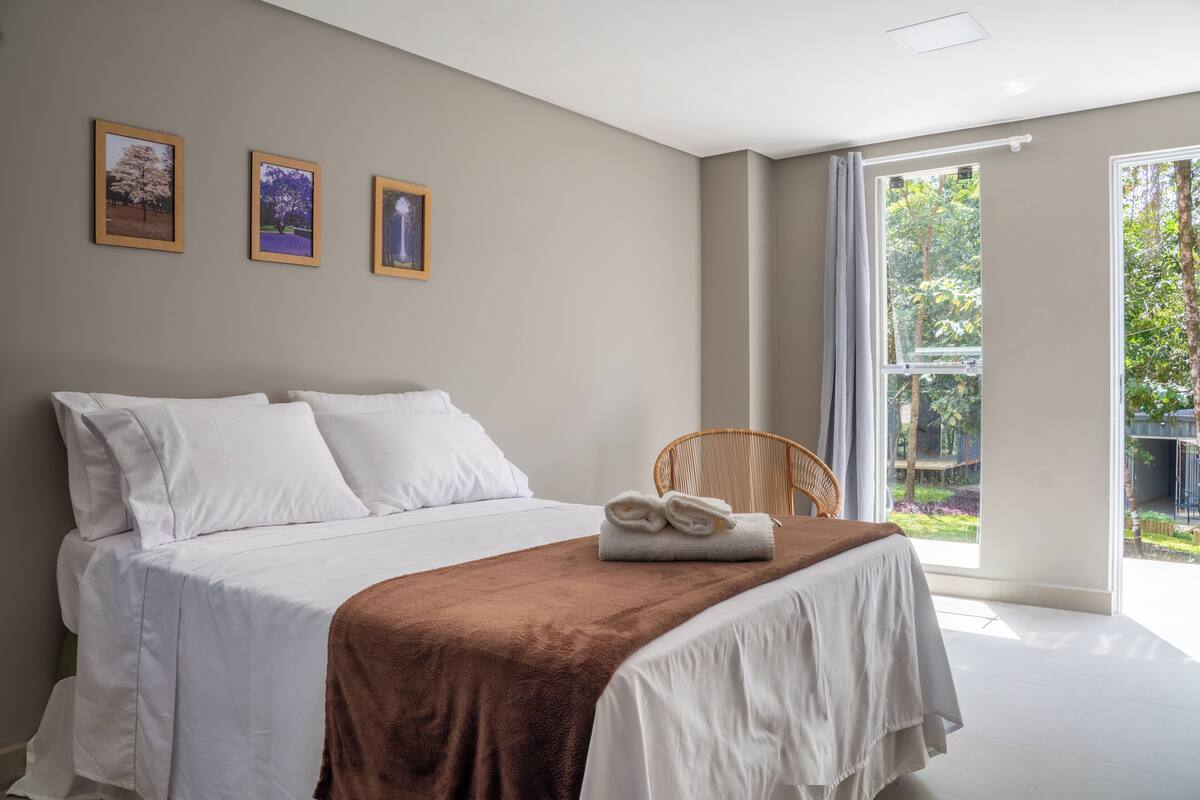 Ein Schlafzimmer mit einem großen Bett, einer braunen Tagesdecke, weißer Bettwäsche und drei gerahmten Bildern an der Wand.