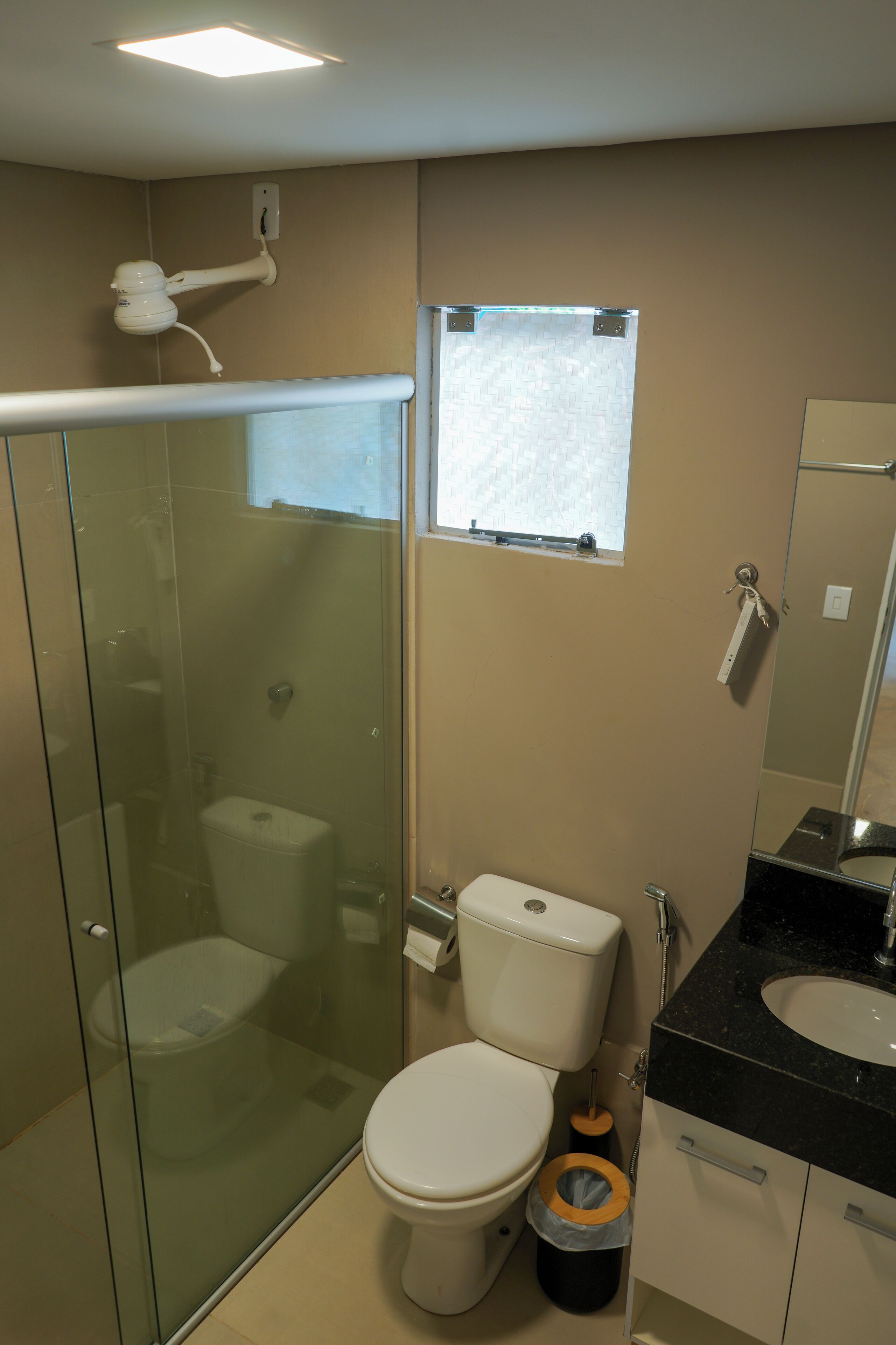A bathroom with a glass-enclosed shower, a toilet, a sink, and a window.