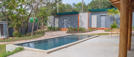 Une piscine agrémentée d’une pergola en bois, entourée d’un jardin où poussent différentes plantes et arbres.