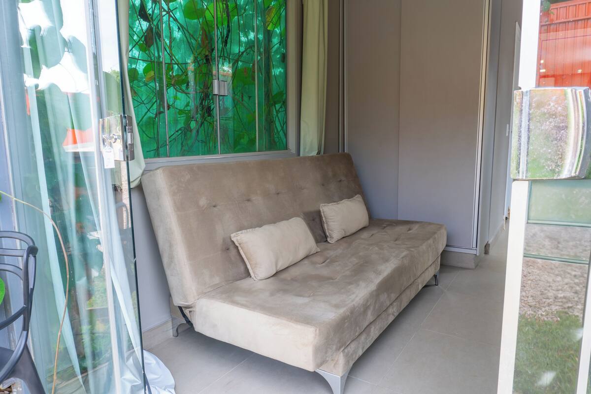 Ein beiges Sofa mit zwei Kissen in einem Raum mit Glastür und Blick auf Grünfläche.