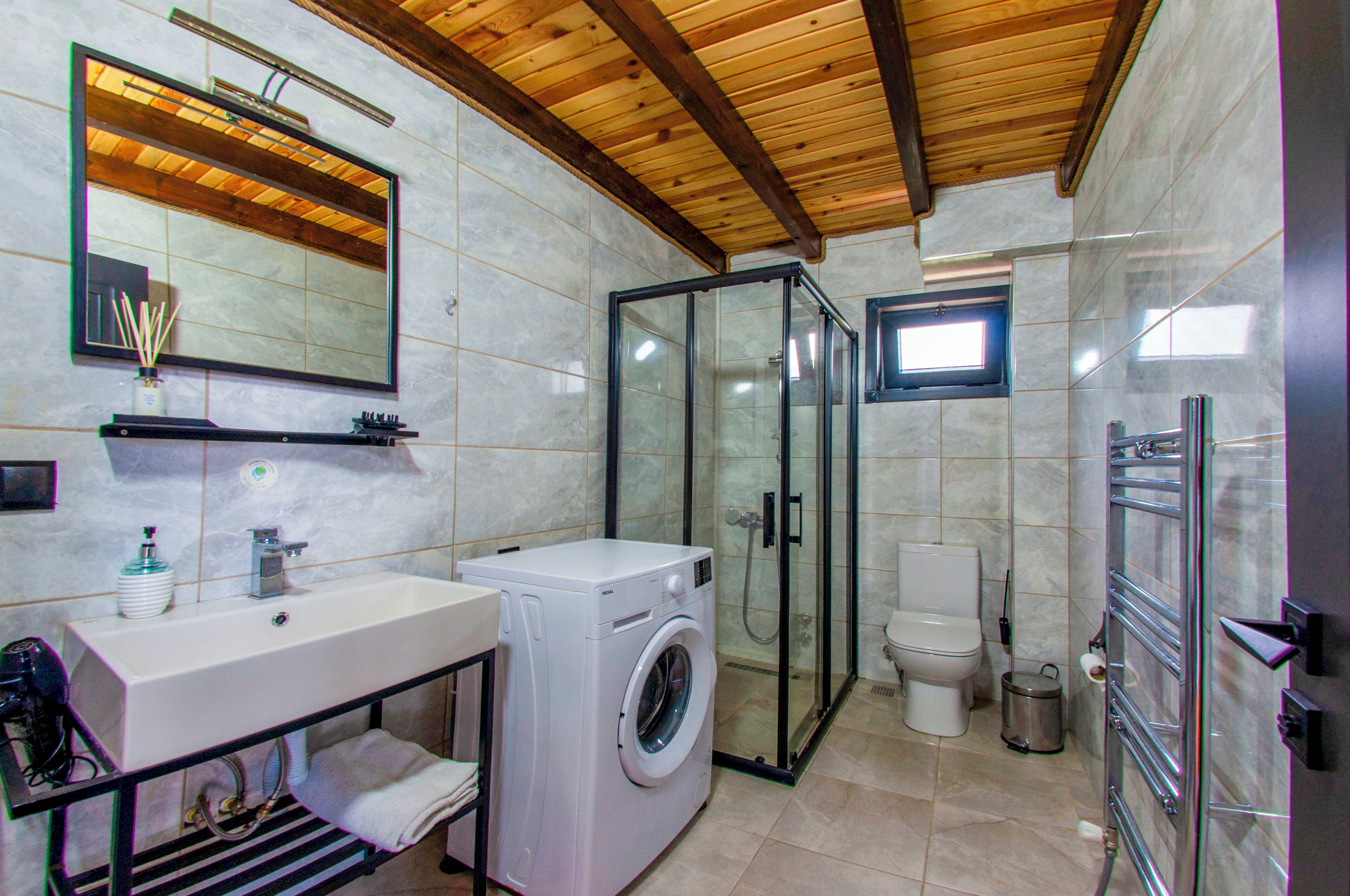 A modern bathroom with a large mirror, a washing machine, a glass-enclosed shower, and a toilet.