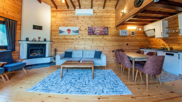 A cozy cabin interior with a fireplace, wooden walls, a dining area, and a living room with a sofa and chairs. - Rubin Sapanca (Sapanca)