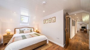 Un dormitorio con cama, mesitas de noche, una ventana y cuadros en la pared.
