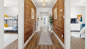A hallway with wooden walls, a central light fixture, and a rug leading to a bedroom with a bed and a dresser.