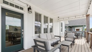 A covered outdoor deck with a gray sofa, a small table, and a chair. - Seabrook's Tori Pines: Hot Tub, Fire Pit, Outdoor Dining, Pet Free! (Pacific Beach)