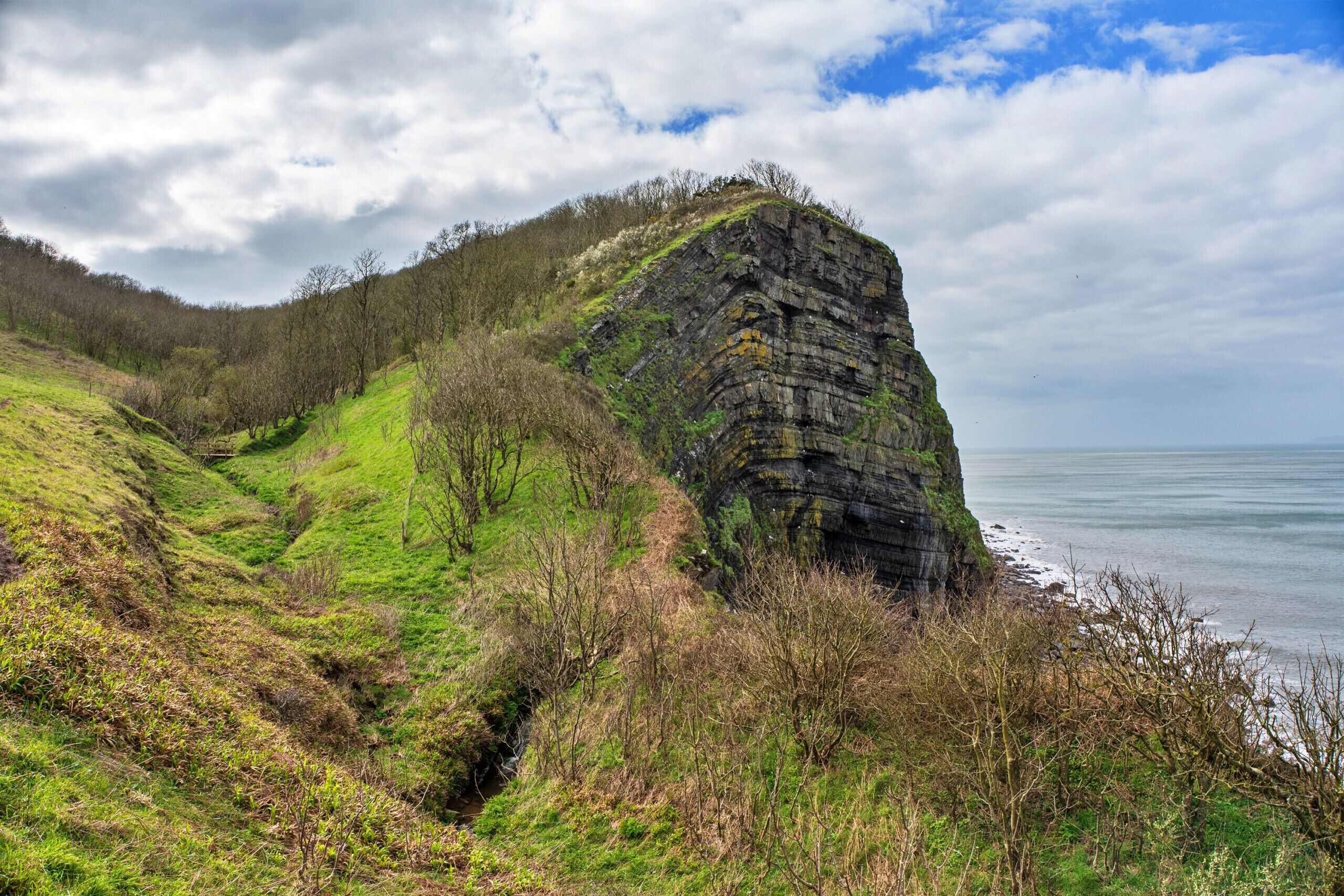 A coastal landscape with a prominent rock formation, a grassy path, and a view of the sea.