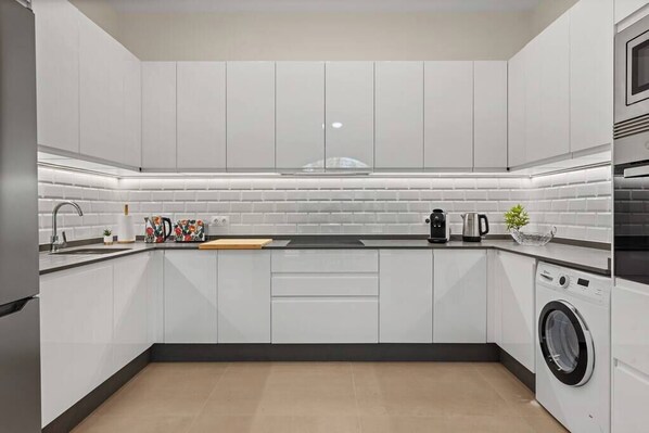 Una cocina moderna con gabinetes blancos, encimera negra y lavadora integrada.