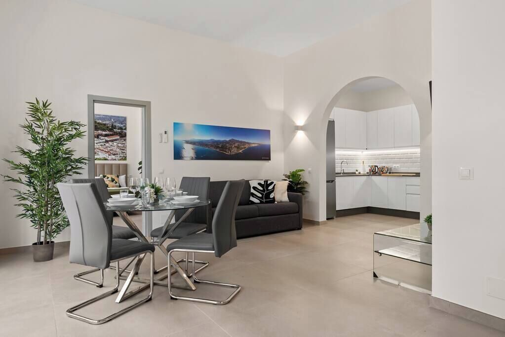 A modern living space with a dining area, a sofa, and a kitchen.