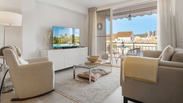 Una sala de estar moderna con televisor de pantalla plana, asientos cómodos, una mesa de centro de vidrio y un balcón con vistas a la ciudad.
