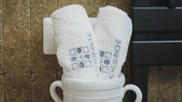 A white ceramic mug with heart-shaped handles containing two white towels with embroidered text.