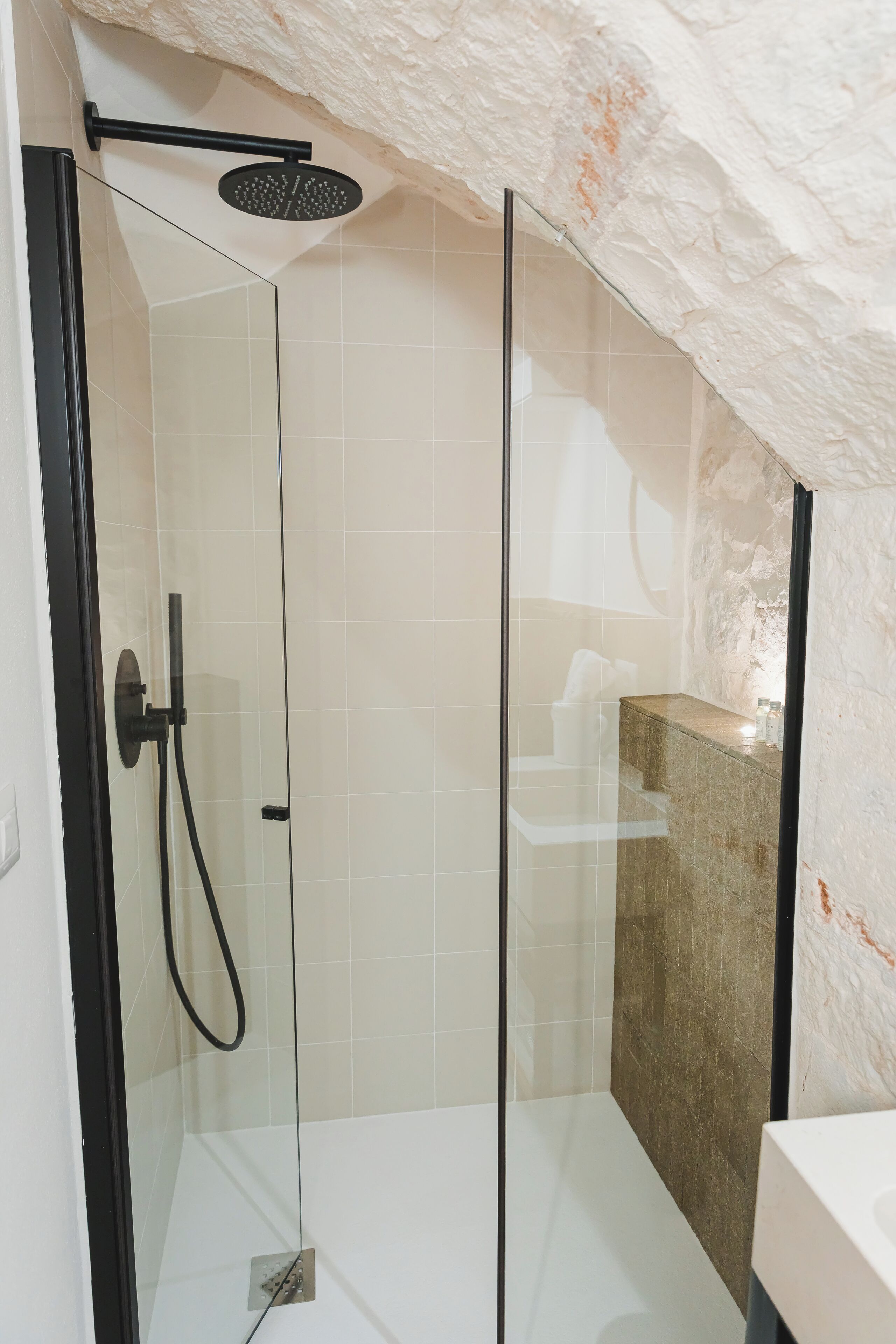 Una ducha con cerramiento de vidrio, cabezal de ducha de mano, panel de control empotrado y tocador con lavabo cubierto de mármol.