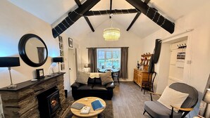 A cozy living room with a fireplace, a dining area with a table and chairs, and a large window with a view. - Riverside Cottage, Abergwynant (sleeps up to 3) - don't forget your binoculars! (Dolgellau)