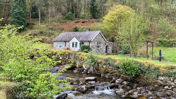 A stone cottage with a thatched roof, surrounded by a lush green landscape and a flowing stream. - Riverside Cottage, Abergwynant (sleeps up to 3) - don't forget your binoculars! (Dolgellau)