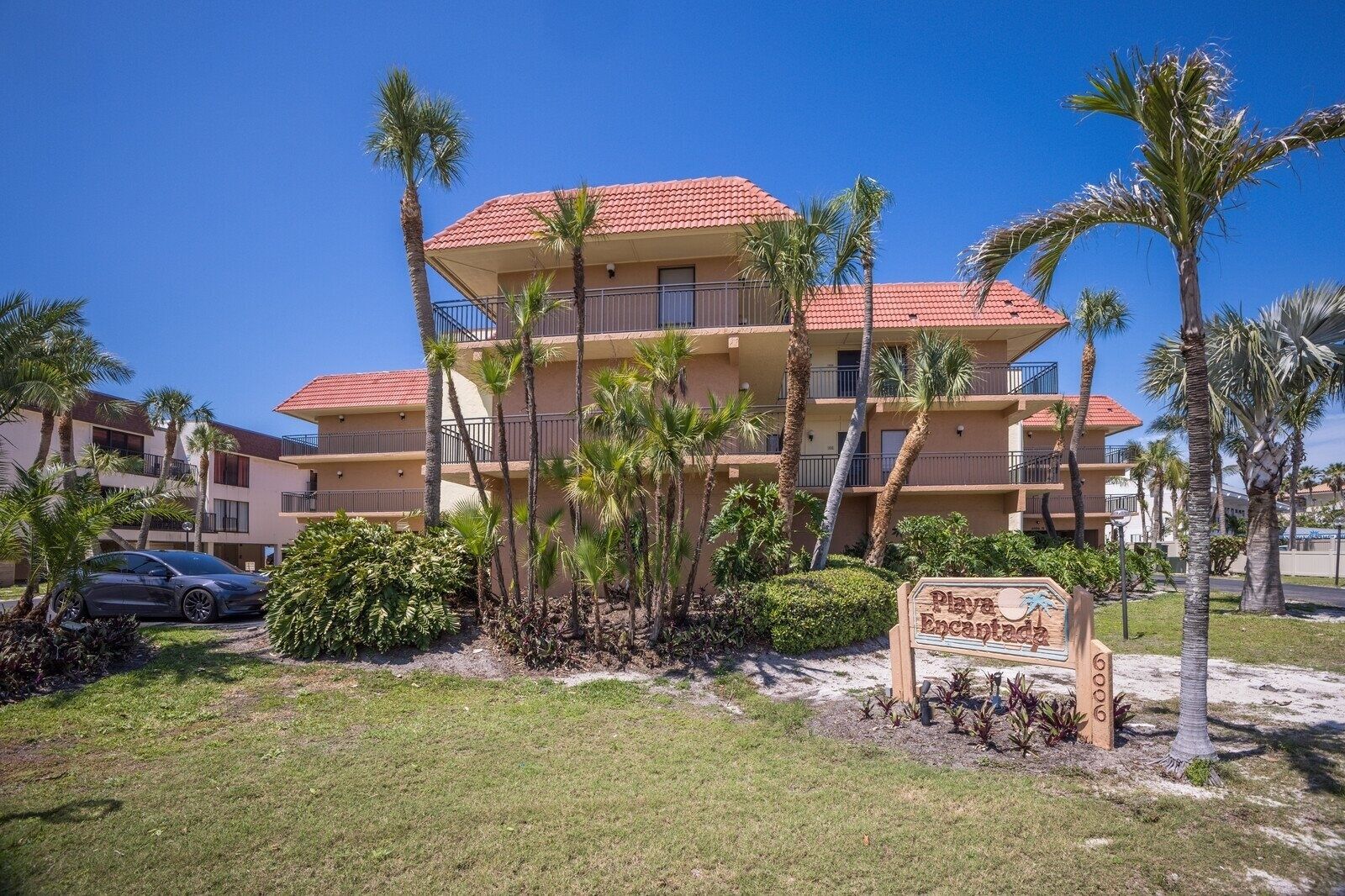 A multi-story hotel with a red-tiled roof, palm trees, and a sign indicating 'Playa Encantada'.