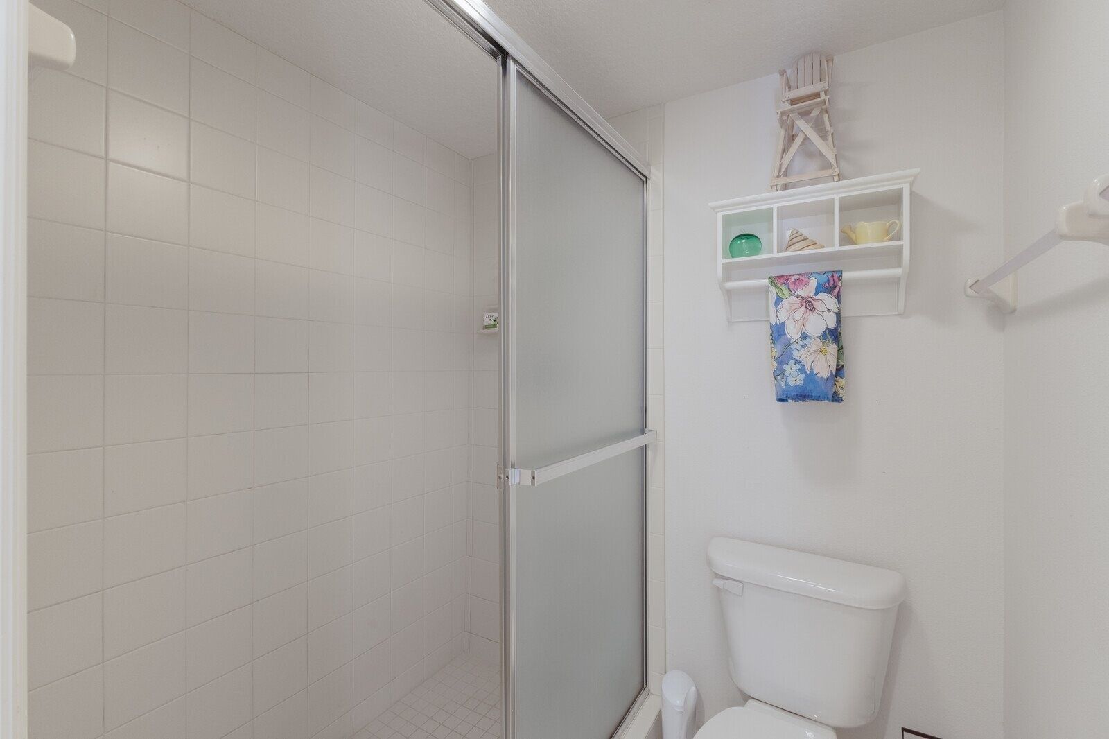 A bathroom with a shower, toilet, and a shelf with toiletries.