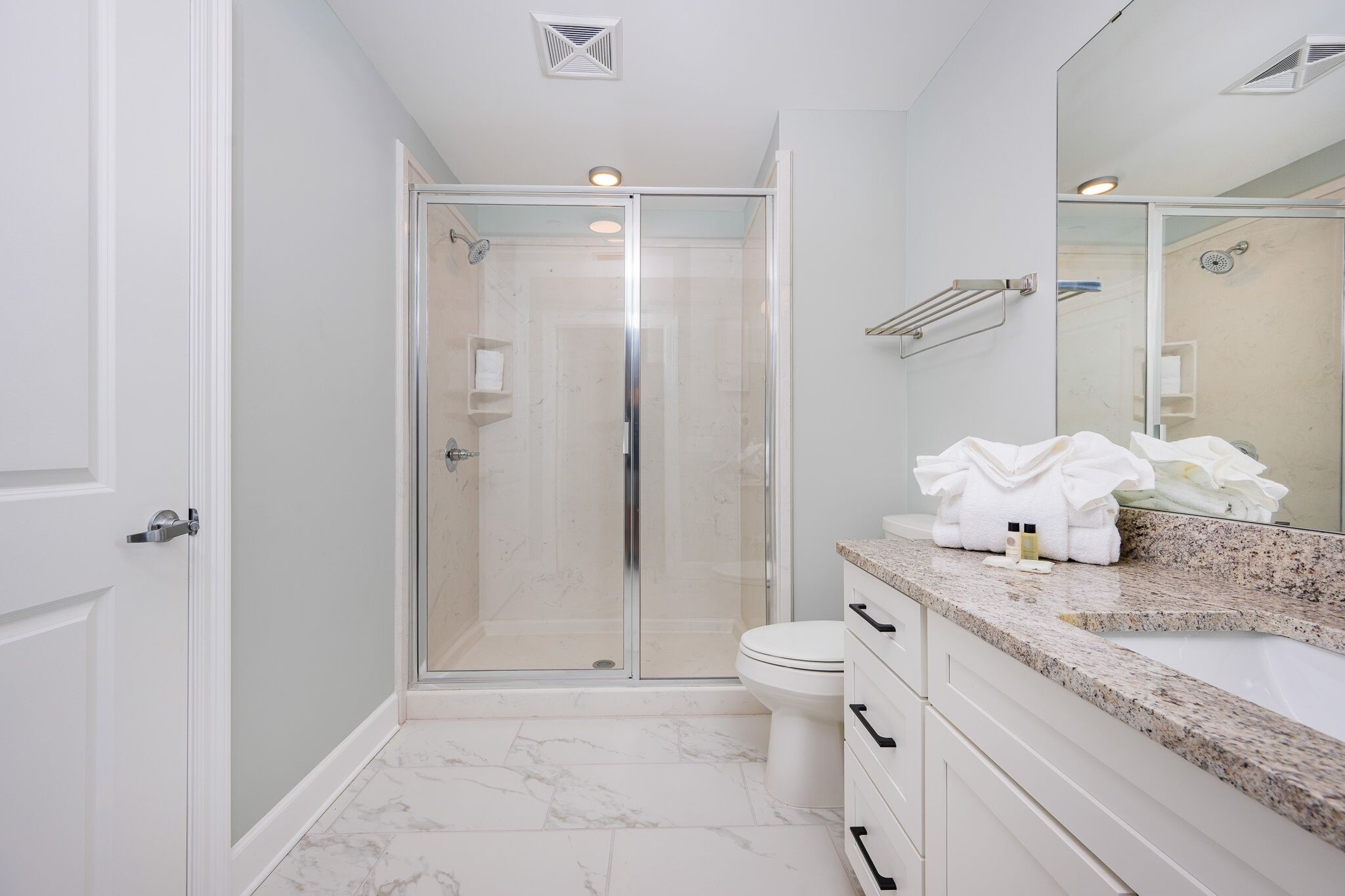 Un baño moderno con cabina de ducha de vidrio, inodoro blanco y encimera de granito con artículos de tocador.