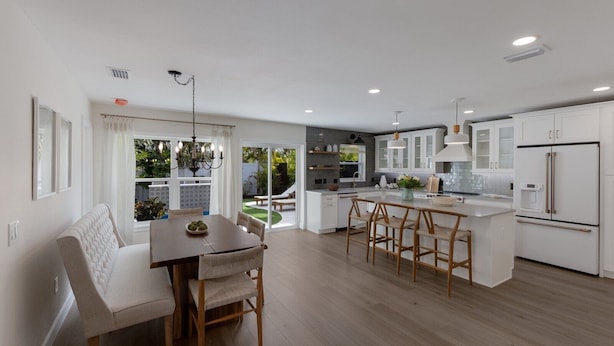 A modern kitchen with white cabinetry, a central island, and a dining area with a bench and chairs. - 83rd St Villas East 2 Bedroom Villa (Holmes Beach)