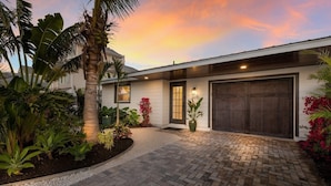 A modern house with a brick driveway, a large garage door, and a well-maintained garden with tropical plants. - 83rd St Villas East 2 Bedroom Villa (Holmes Beach)