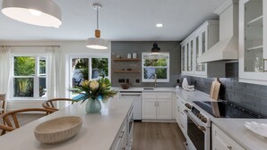 A modern kitchen with white cabinetry, a central island, and a view of greenery outside. - 83rd St Villas East 2 Bedroom Villa (Holmes Beach)
