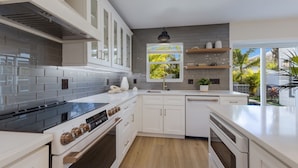 A modern kitchen with white cabinetry, a black stove, and a window with a view of greenery. - 83rd St Villas West 2 Bedroom Villa (Holmes Beach)
