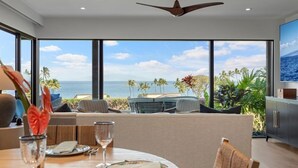 A modern dining area with a view of the ocean, a ceiling fan, and a dining table set with plates and glasses. - Wailea Elua 2007 1 Bedroom Condo (Kihei)