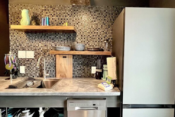 A kitchen with a marble countertop, a stainless steel sink, a wooden shelf, and a refrigerator. - Beachview 326 Studio (Gulf Shores)