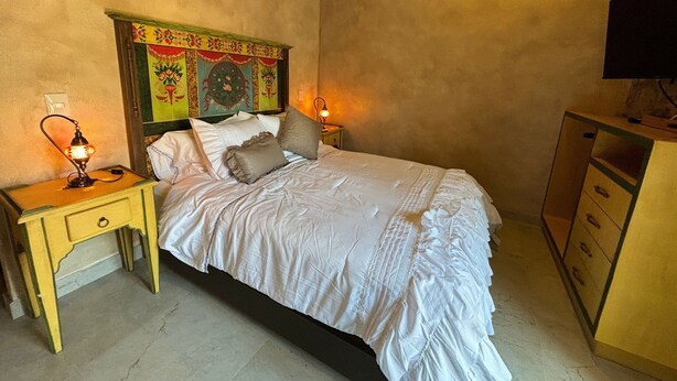 A bedroom with a bed, two bedside tables, a nightstand, a television, and a wall with a decorative panel.