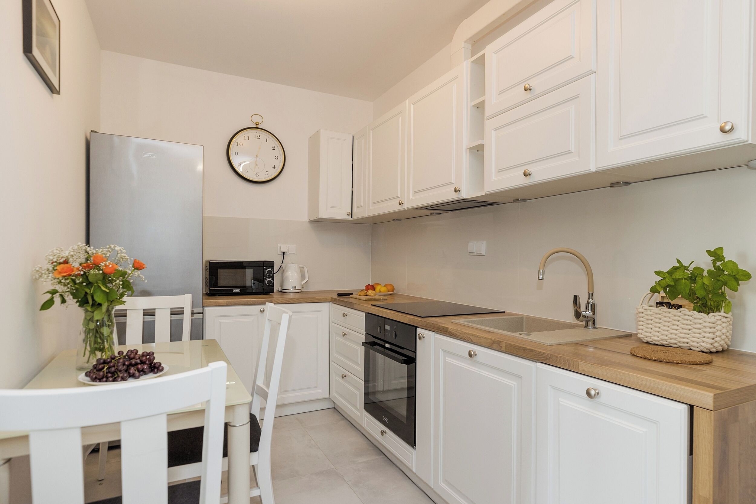 Una cucina moderna con mobili bianchi, un frigorifero in acciaio inossidabile, un forno a microonde, un forno e un lavello.