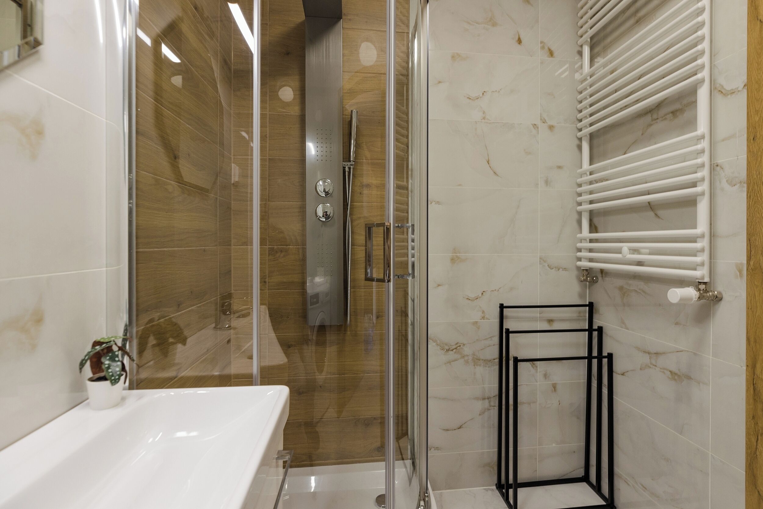 A modern bathroom with a glass shower enclosure, a white sink, and a marble-tiled wall.
