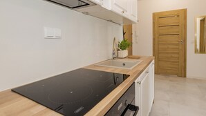 Ett modernt kök med en svart induktionshäll, vita skåp, en trädörr och en liten krukväxt på bänkskivan.