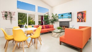 Uma sala de estar moderna com sofás laranja, cadeiras amarelas, uma mesa de centro de vidro e uma lareira.