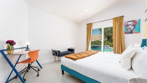 Quarto de hotel moderno com cama, escrivaninha e cadeira. Há uma janela com cortinas, um vaso com flores e um quadro na parede.
