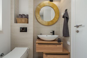 Een moderne badkamer met een witte wastafel, houten opbergmeubel, een ronde spiegel en een handdoekrek.