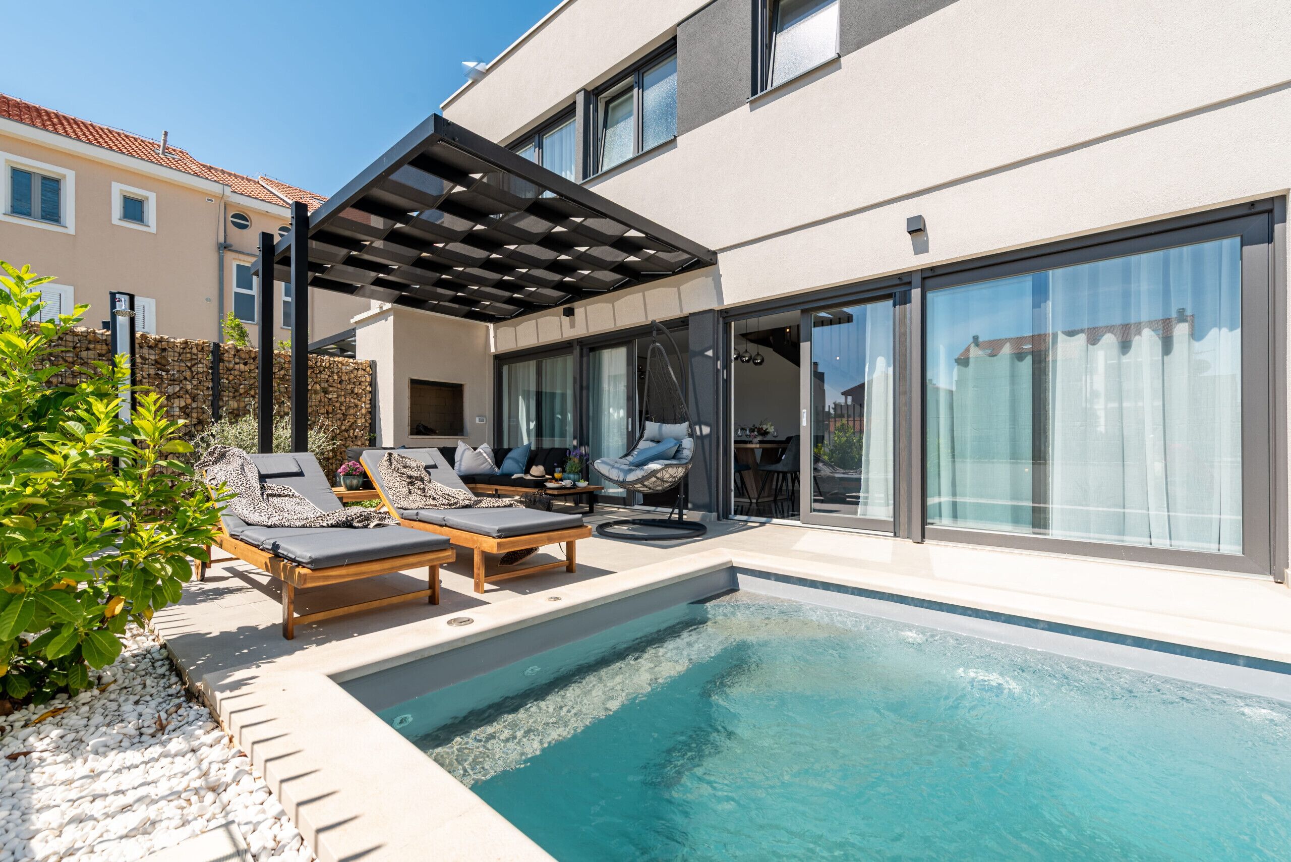 Ein moderner Poolbereich im Freien mit Liegestühlen und einer Pergola.