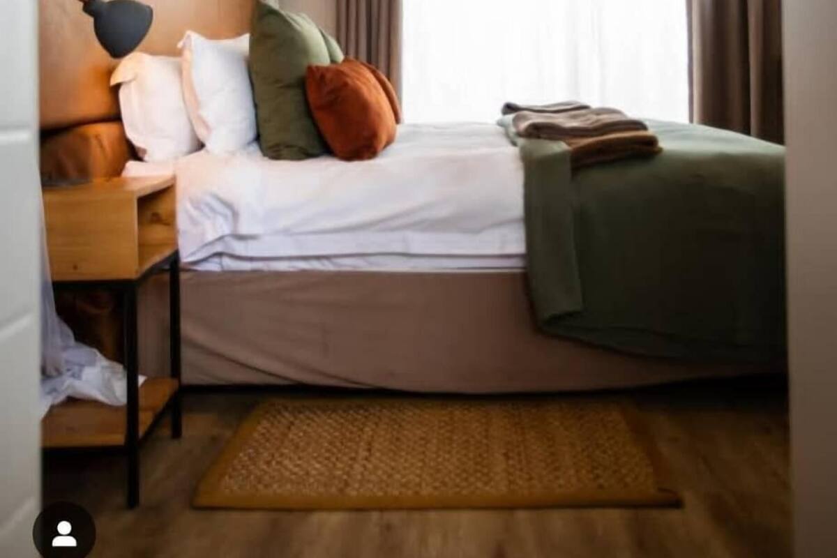 Camera d'albergo ordinata con un letto, comodino, lampada e vista sull'esterno dalla finestra.