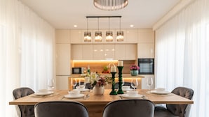 A modern dining area with a wooden table set for four, surrounded by dark upholstered chairs. A kitchen is visible in the background with a warm light. - Villa Mia Zadar Villas (Privlaka)