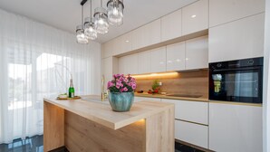 A modern kitchen with a wooden island, white cabinets, a black oven, and a pendant light fixture. - Villa Mia Zadar Villas (Privlaka)