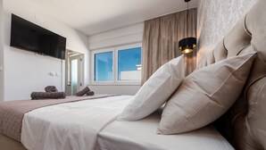 A bedroom with a large bed, a flat-screen TV mounted on the wall, a window with curtains, and a bedside lamp. - Villa Mia Zadar Villas (Privlaka)