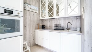 A modern kitchen with white cabinets, a built-in oven, a coffee maker, and a sink with a faucet. - Apartamenty Sun & Snow Nad Zalewem (Dziwnówek)