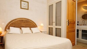 A bedroom with a large bed, a wooden wardrobe, and a small bedside table with a lamp. - Gîte Amandier - in the Provencal farmhouse of Domaine Faverot (Maubec)