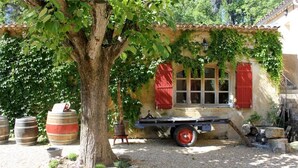 A rustic building with a tree in front, barrels, and a flatbed trailer. - Gîte Amandier - in the Provencal farmhouse of Domaine Faverot (Maubec)