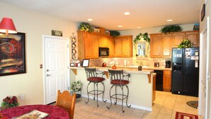 A kitchen with wooden cabinets, a black refrigerator, a dining area with a red tablecloth, and a red lamp.