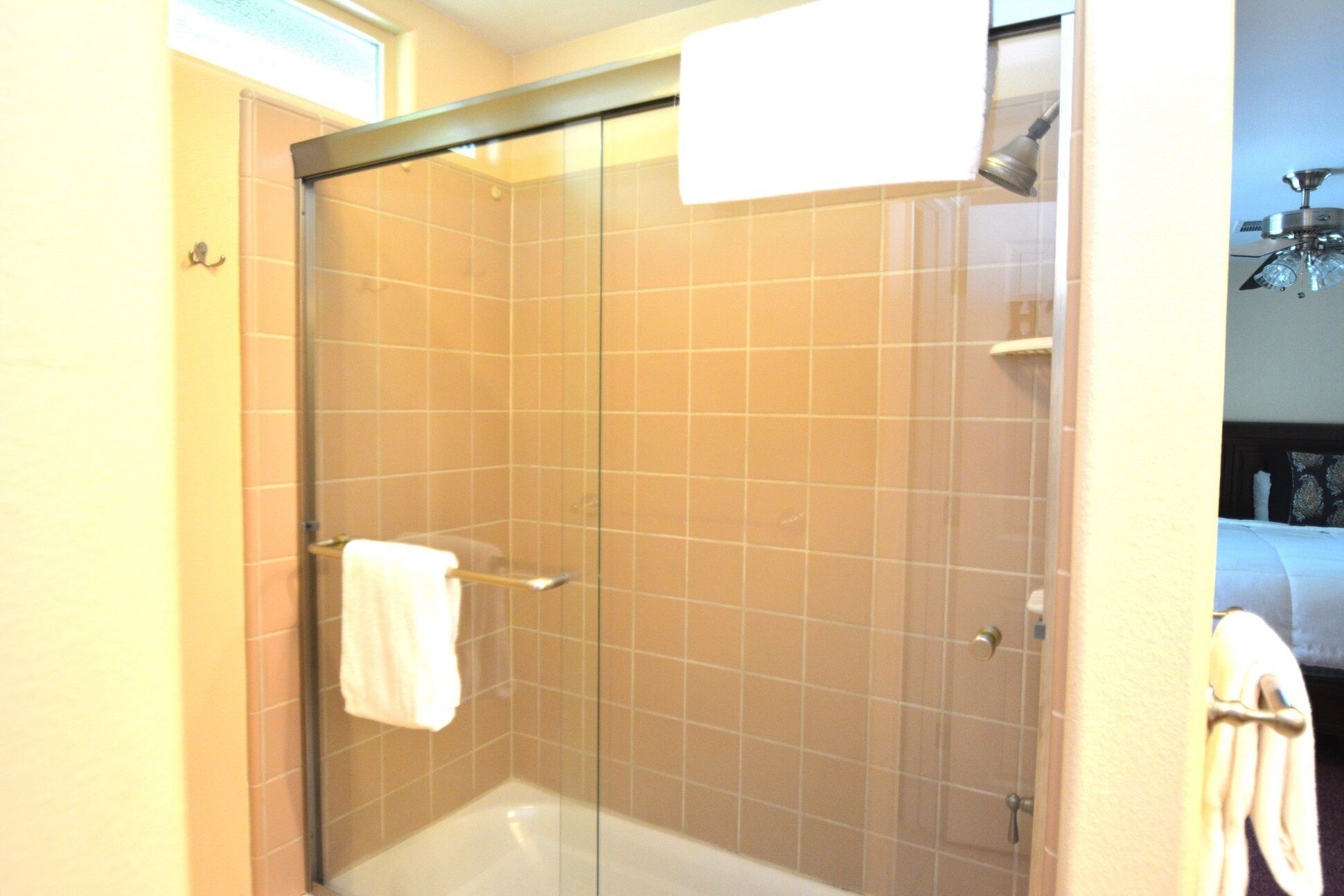 A glass-enclosed shower with beige tiles, a white towel on the door handle, and a visible showerhead.