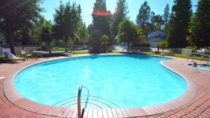 A swimming pool with a brick deck, surrounded by trees and a fence.