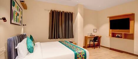 Habitación de hotel con cama, escritorio, silla, televisor y ventilador de techo.