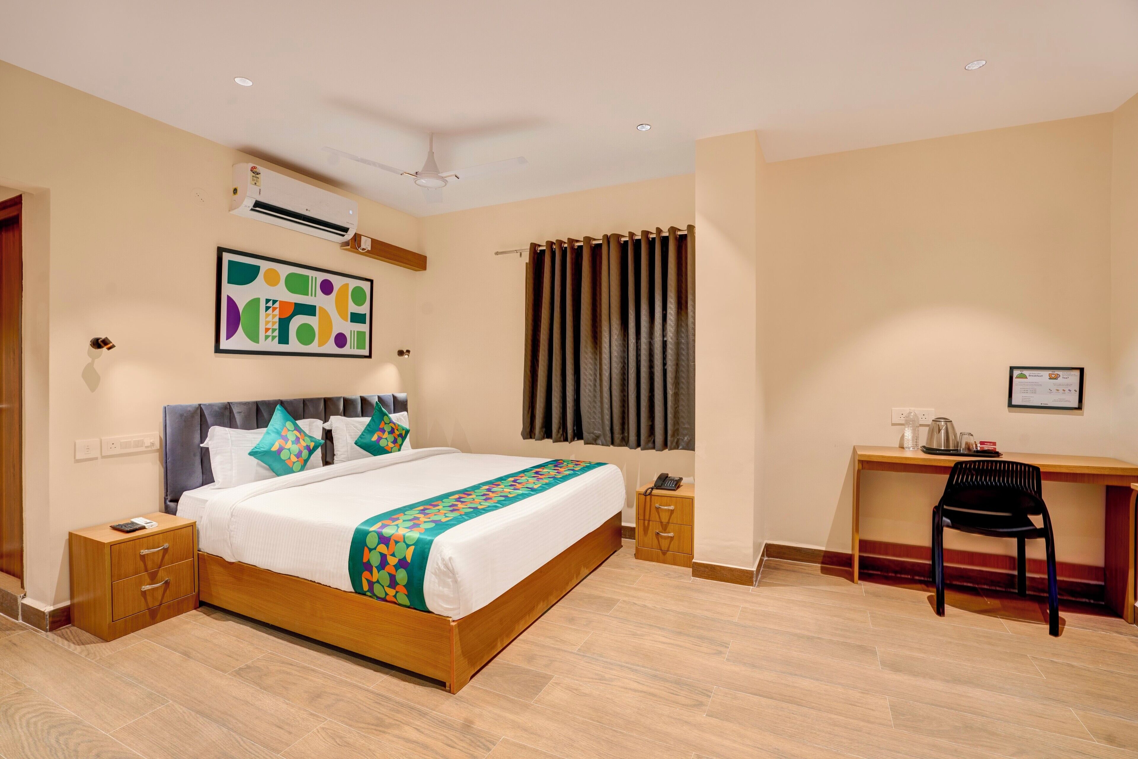 Une chambre d’hôtel avec un lit en bois, un bureau, une chaise, un climatiseur et un ventilateur de plafond.