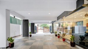 A modern hotel corridor with patterned flooring, potted plants, and a glass wall on one side. - Treebo Address Inn Gachibowli (Hyderabad)