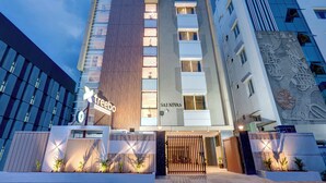 Un hotel moderno con un llamativo letrero con forma de árbol, un panel de madera vertical y el rótulo 'SAI NIVAS' en la fachada.