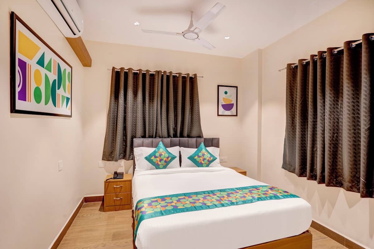 A bedroom with a bed, curtains, a ceiling fan, a bedside table, and a wall-mounted air conditioner.