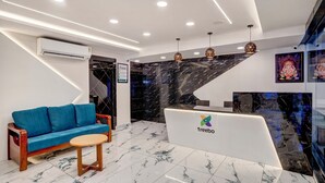 A modern reception area with a marble floor, a blue sofa, a round wooden table, and a reception desk with the logo 'treebo'. - Treebo Address Inn Gachibowli (Hyderabad)